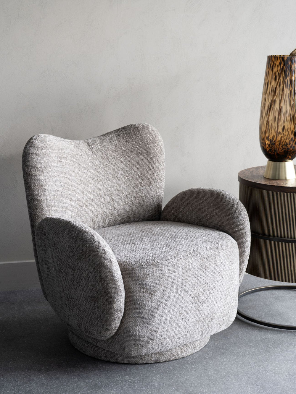 Gray armchair in a minimalistic room with a lamp on a side table.