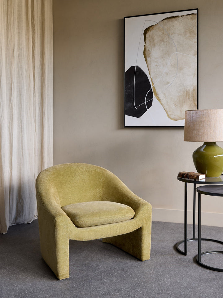 Yellow armchair in a room with abstract art and a lamp.