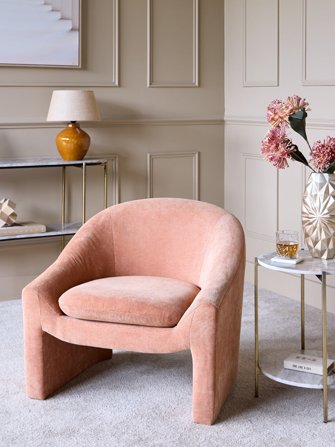 Pink armchair in a stylish living room with a side table and lamp.