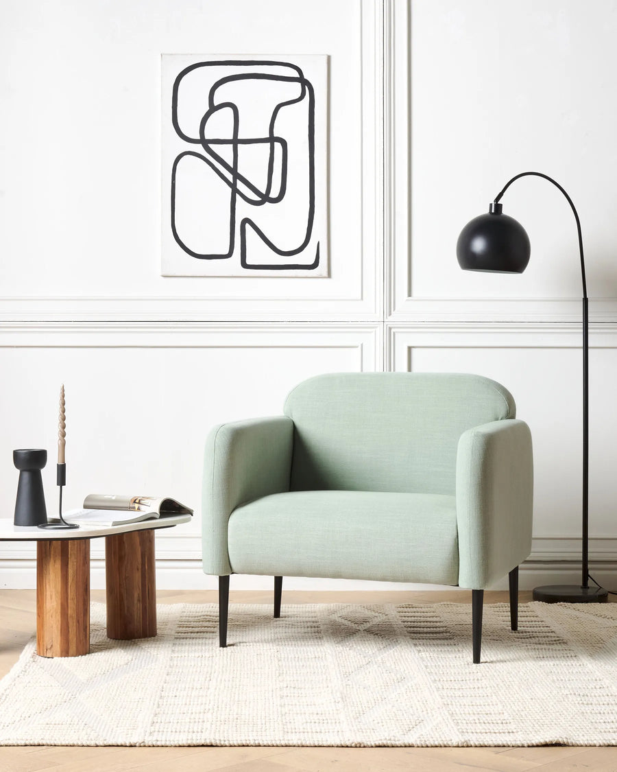 Modern living room with a light green armchair, wooden coffee table, and abstract wall art.