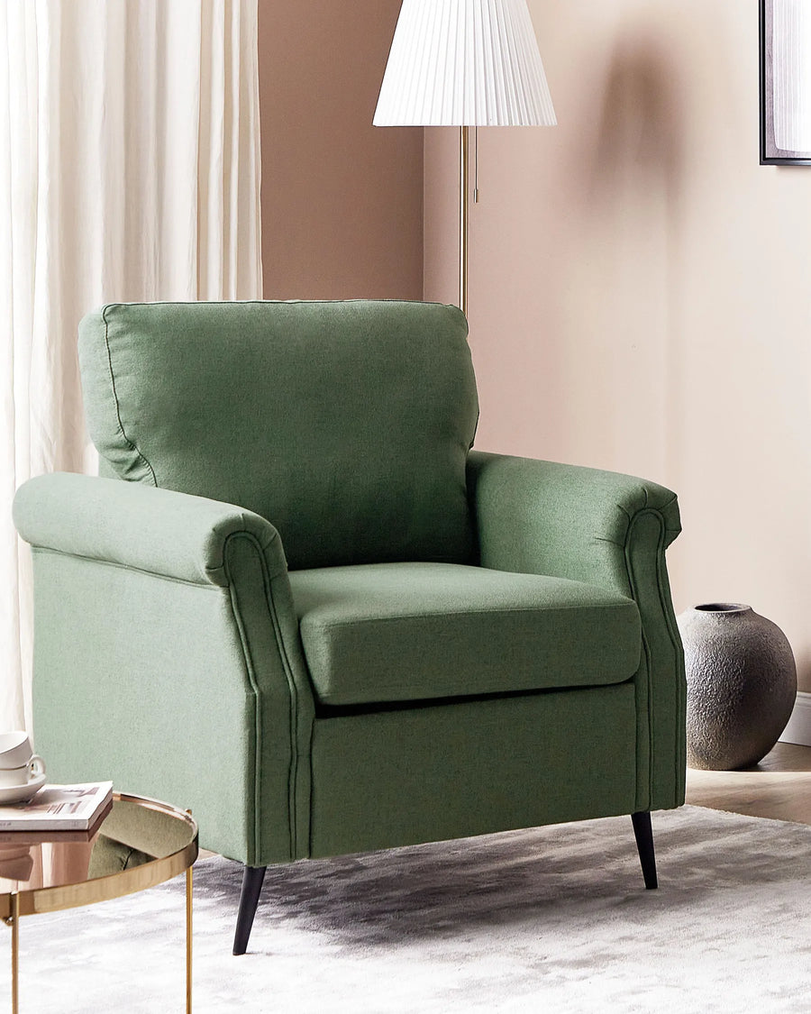 Green armchair in a living room setting with a lamp and vase in the background.