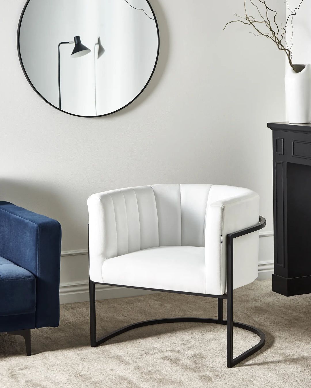 White armchair in a room with a blue chair, mirror, and black cabinet.