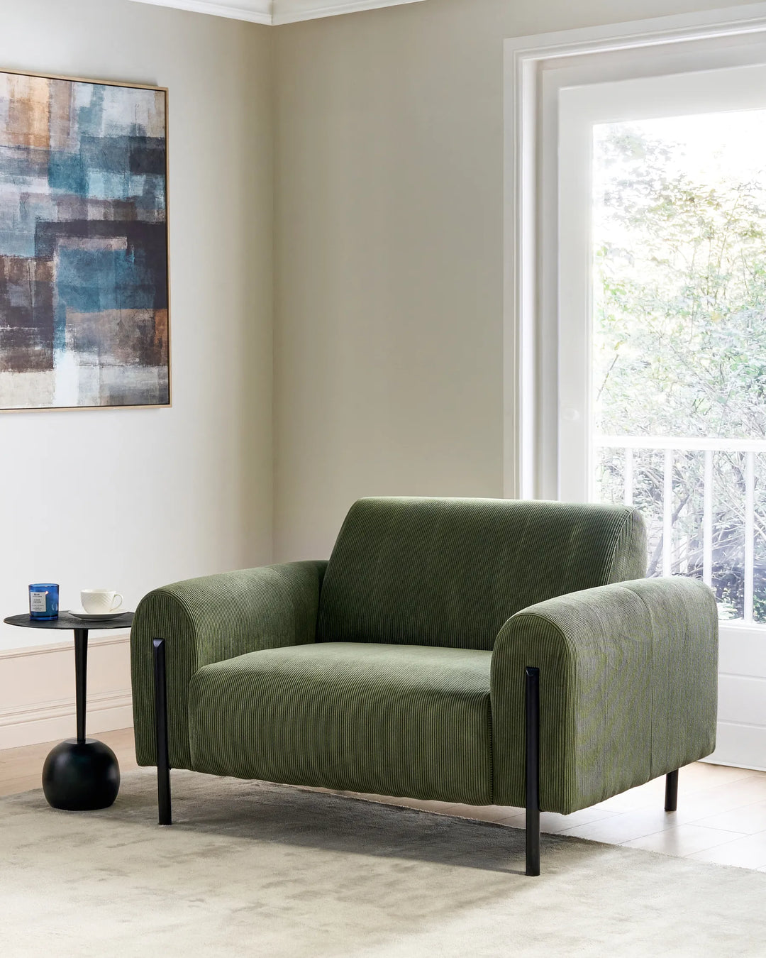 Green armchair in a living room with abstract art and a window in the background