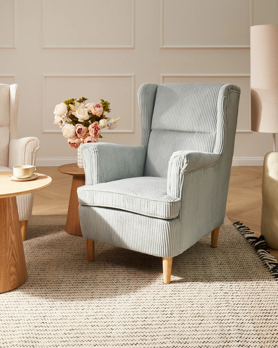 Light blue armchair in a living room setting with a coffee table and flowers.