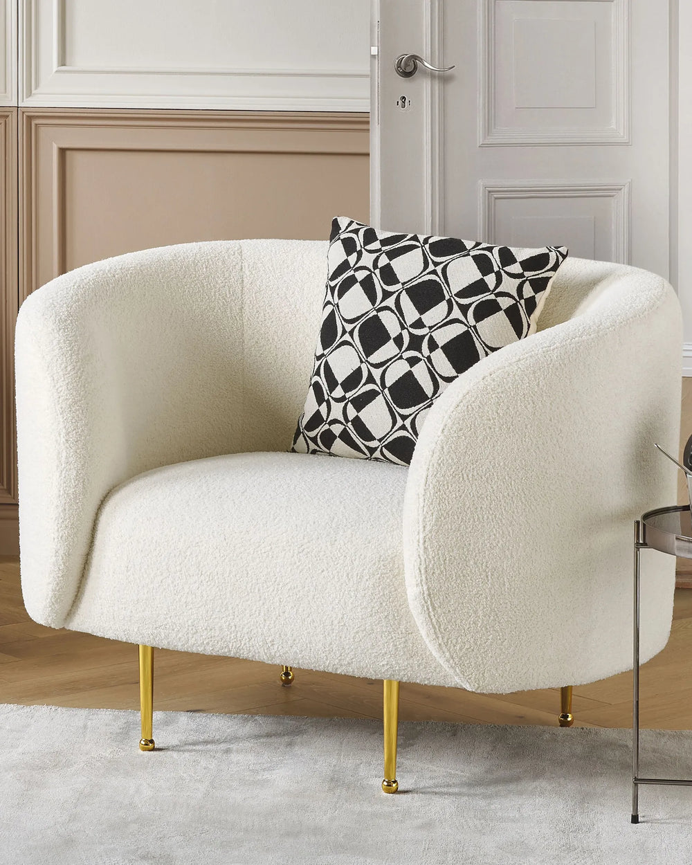 White armchair with gold legs and a black and white patterned pillow in a room.