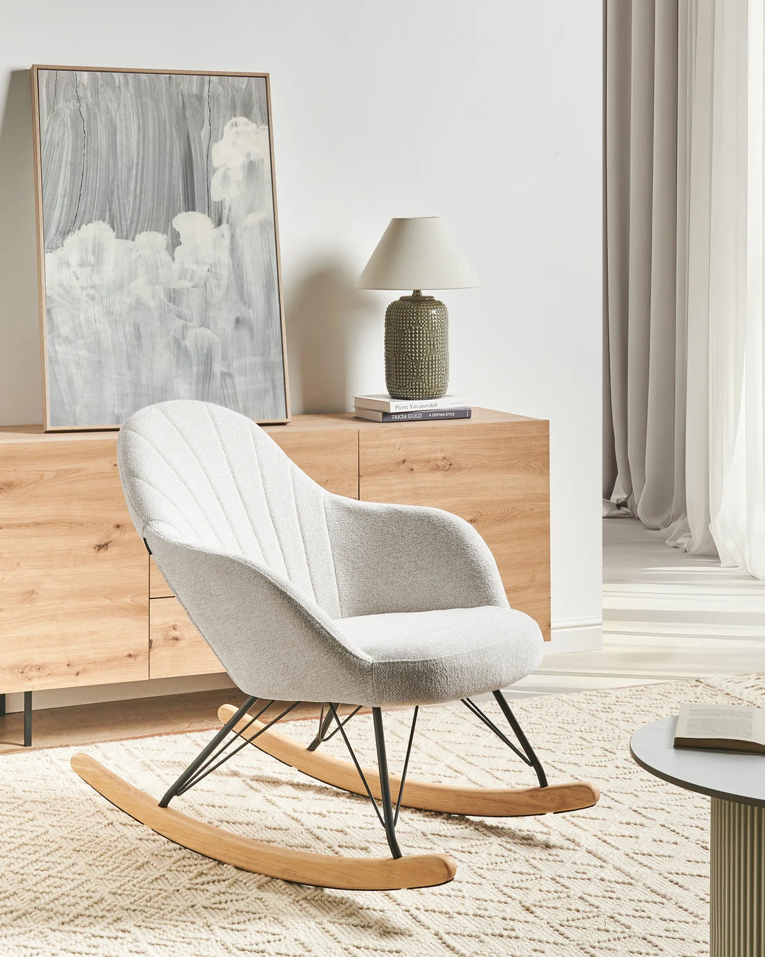 Gray rocking chair in a modern living room with wooden cabinet and abstract art.