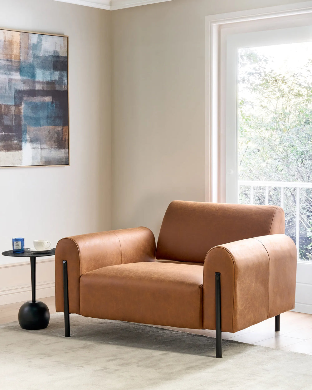 Brown leather armchair in a modern living room with abstract art and a window.