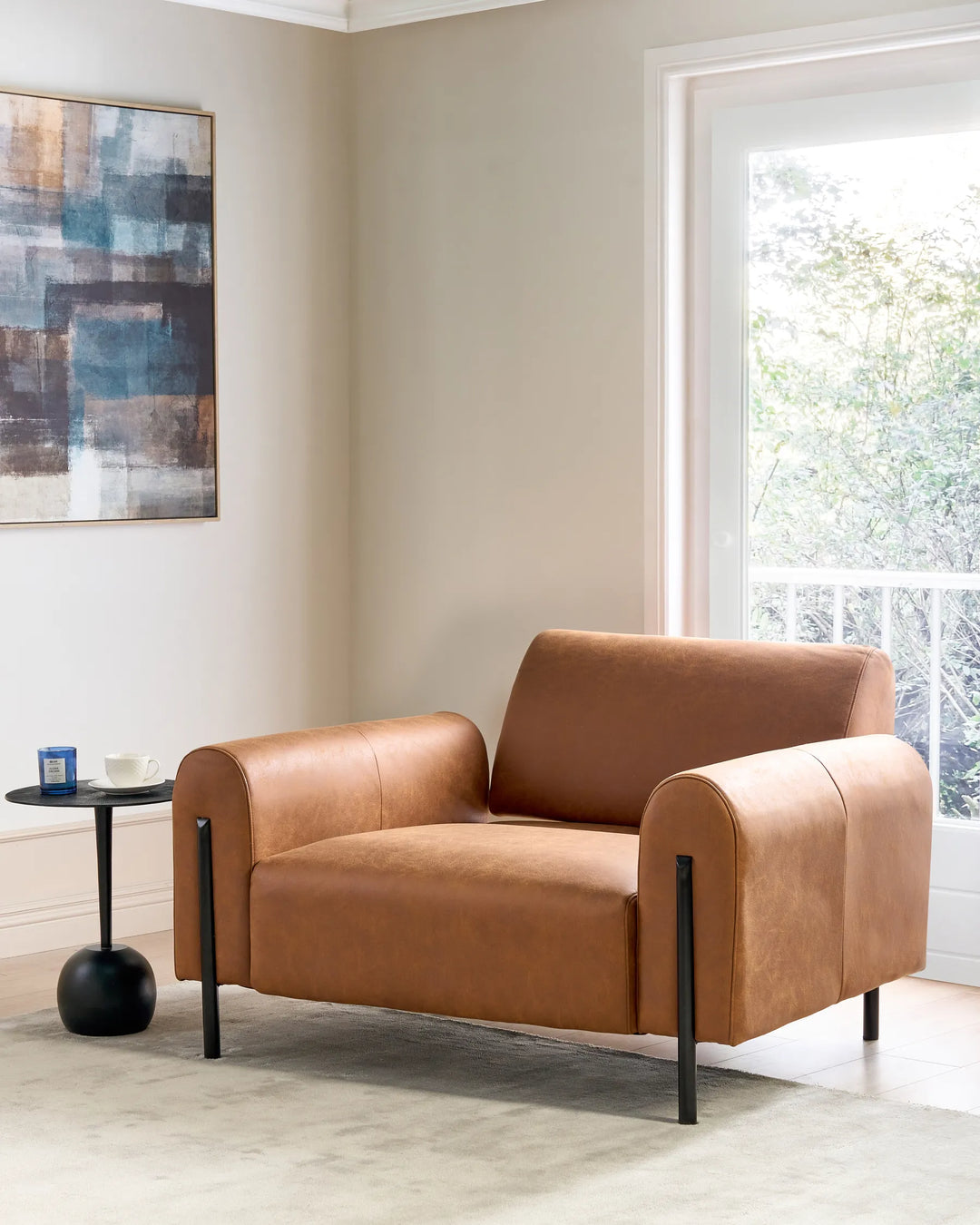 Brown leather armchair in a modern living room with abstract art and a window.