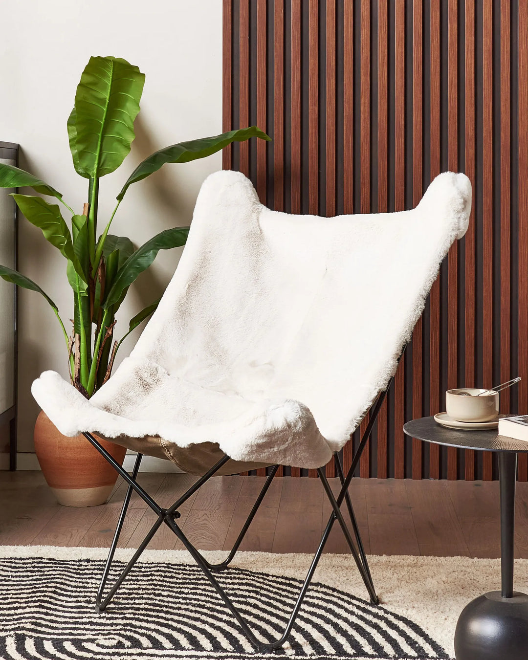 White fur-covered chair in a room with a plant and small table.