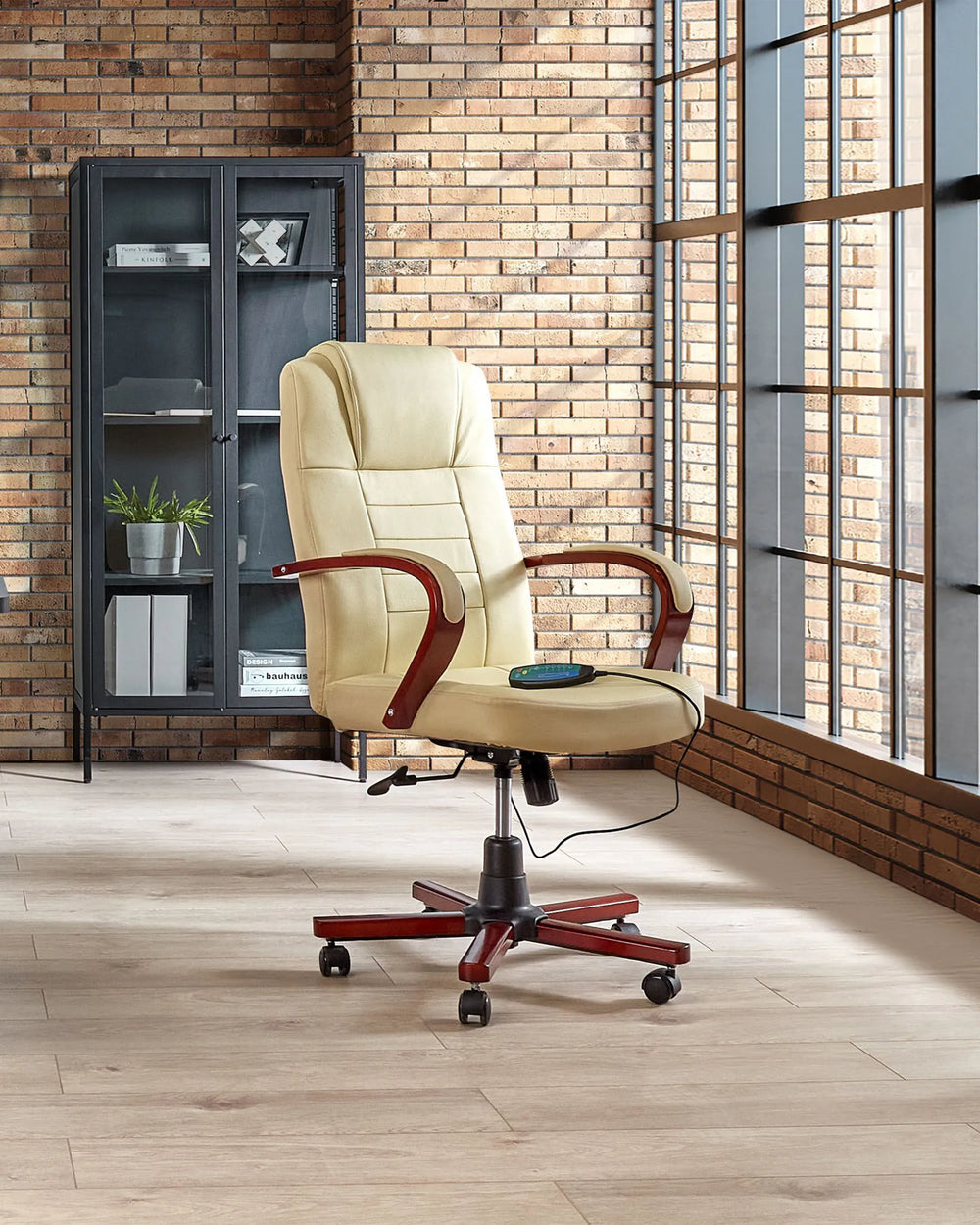 Beige office chair with wooden armrests in a room with brick walls and large windows.
