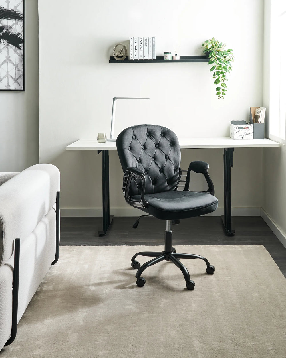 Gray office chair in front of a white desk with a plant and books on a shelf.