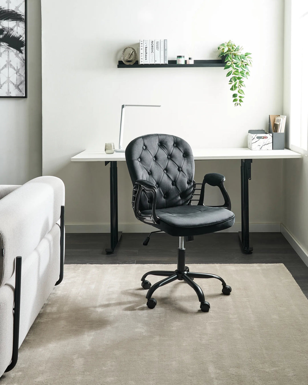Gray office chair in front of a white desk with a plant and books on a shelf.