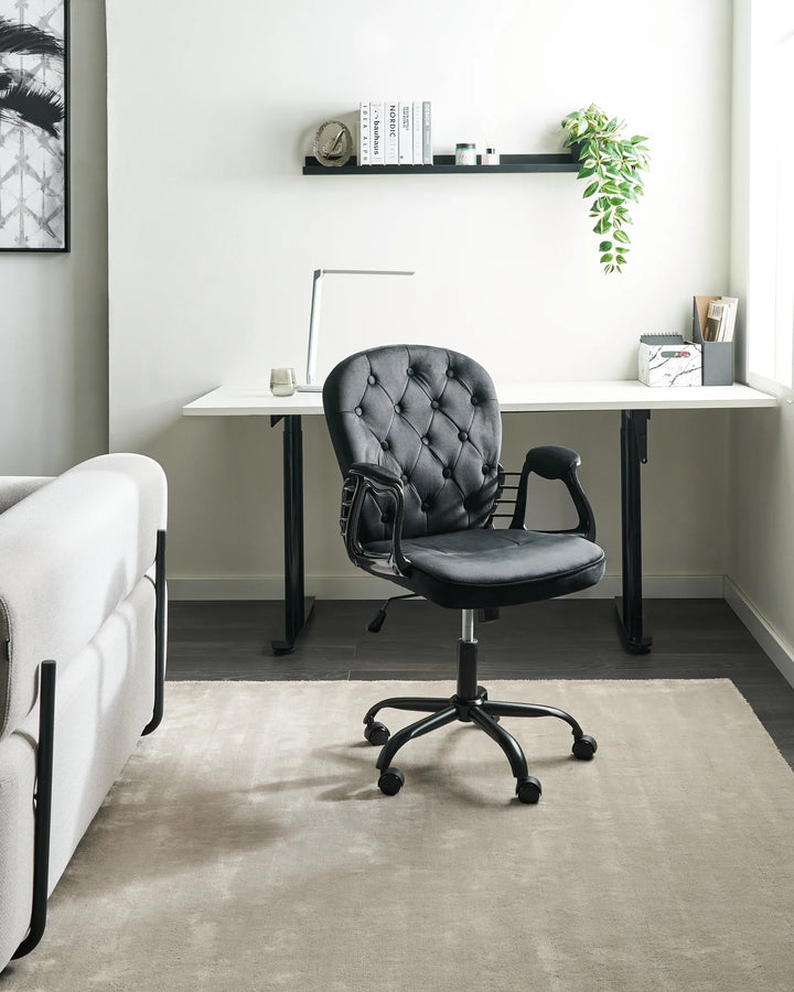 Gray office chair in front of a white desk with a plant and books on a shelf.