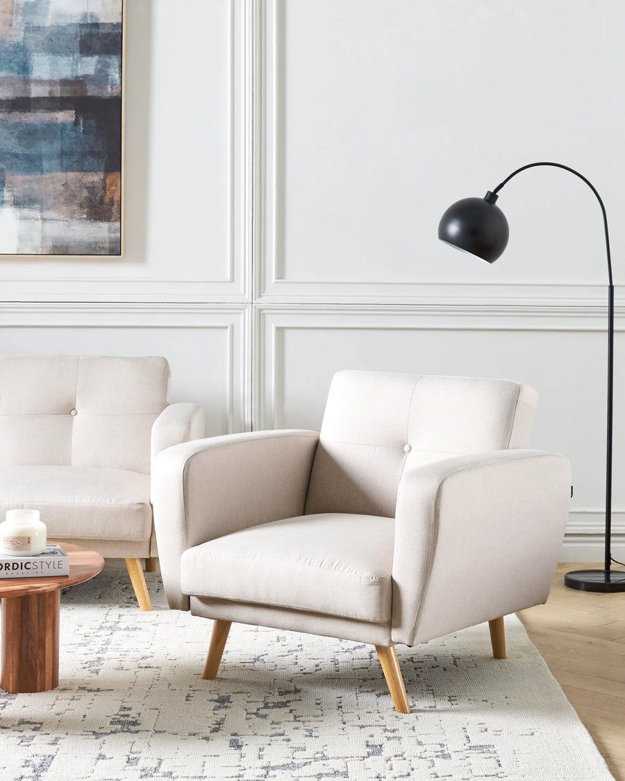 Beige armchair in a modern living room with a white wall and black floor lamp.