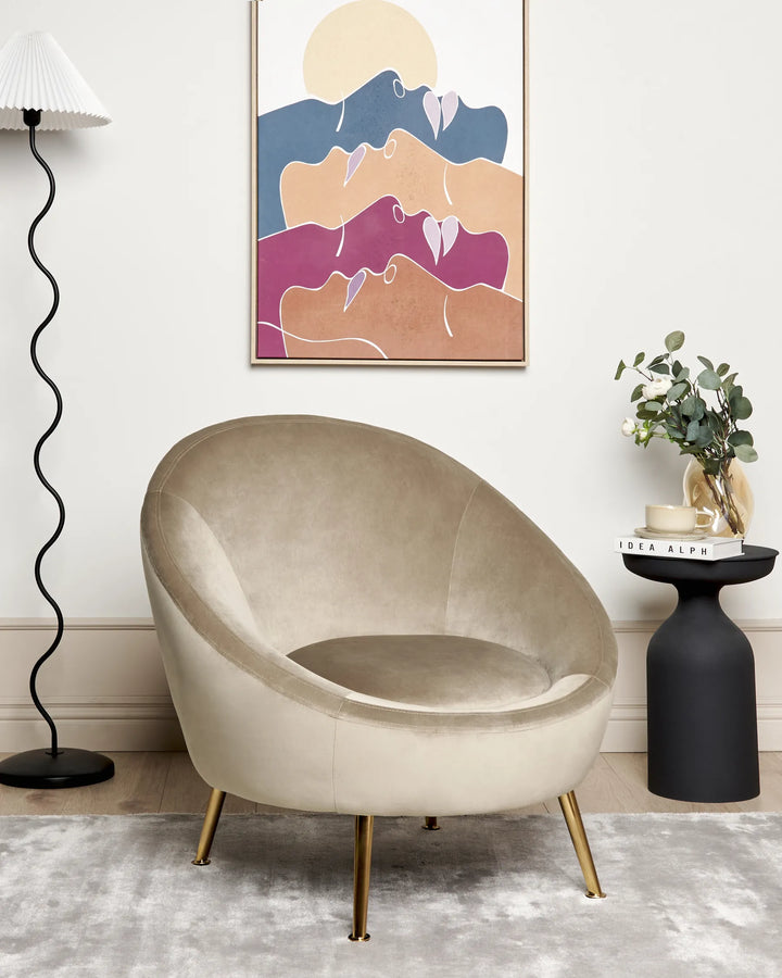 Beige armchair in a modern living room with abstract art and a lamp.