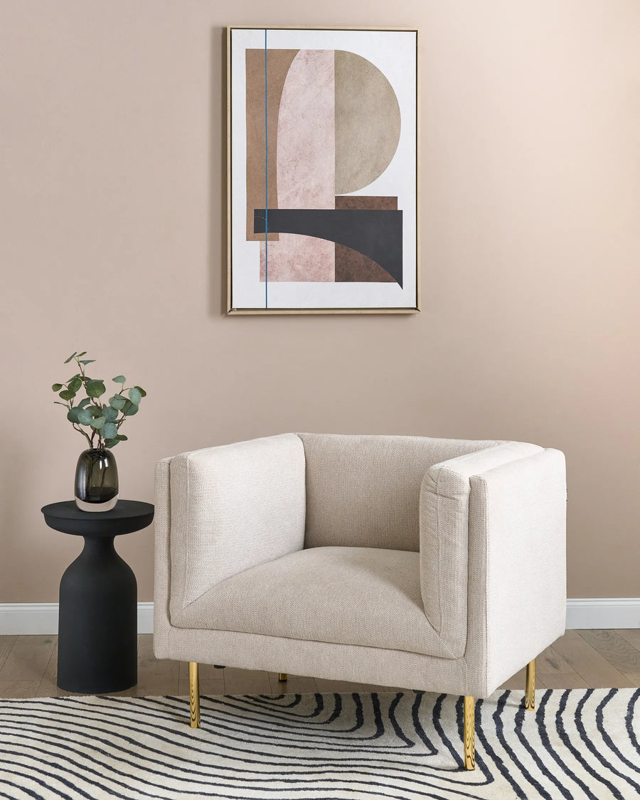 Beige armchair in a room with abstract art and a black side table.