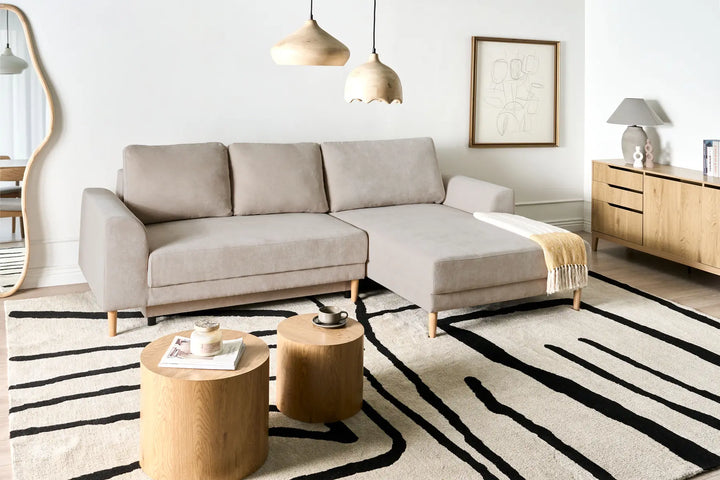 Modern living room with a beige sectional sofa, wooden coffee table, and striped rug.