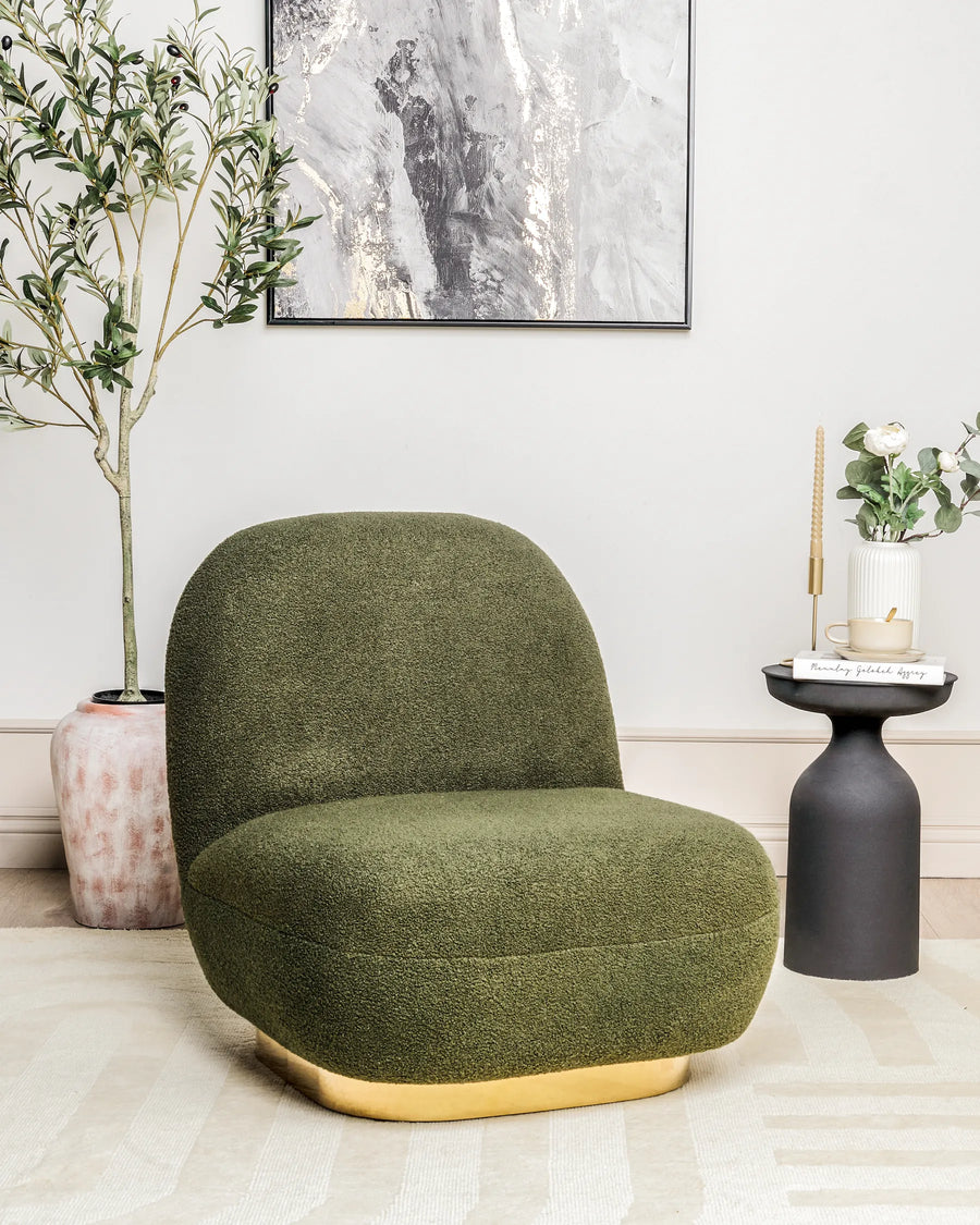 Green armchair with gold base in a room with plants and a painting.