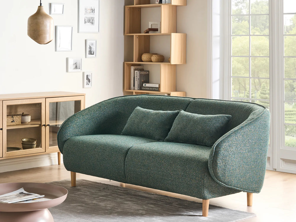Green sofa in a living room with wooden bookshelf and window