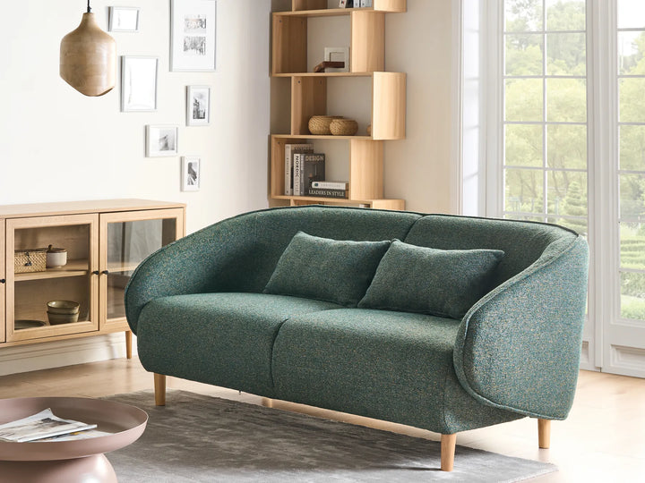 Green sofa in a living room with wooden bookshelf and window