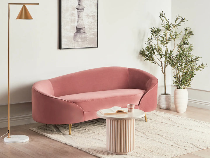 Modern living room with a pink sofa, round table, and decorative plants.