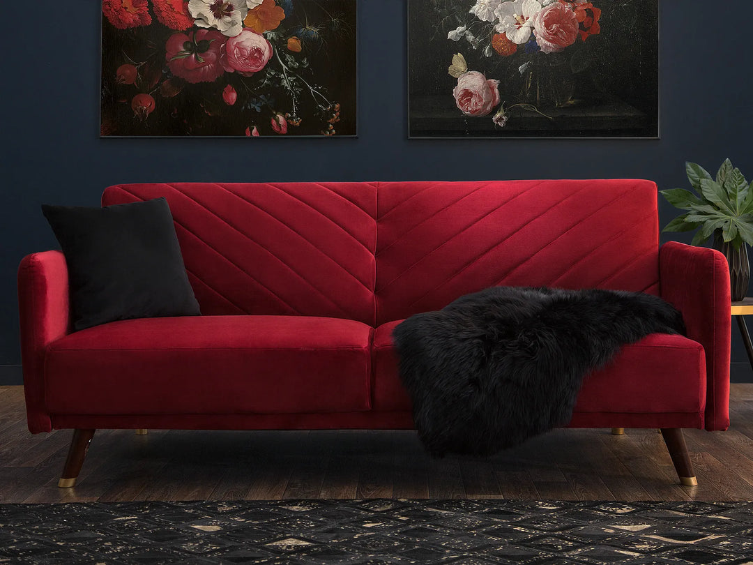 Red sofa with a black throw blanket in a room with floral wall art.