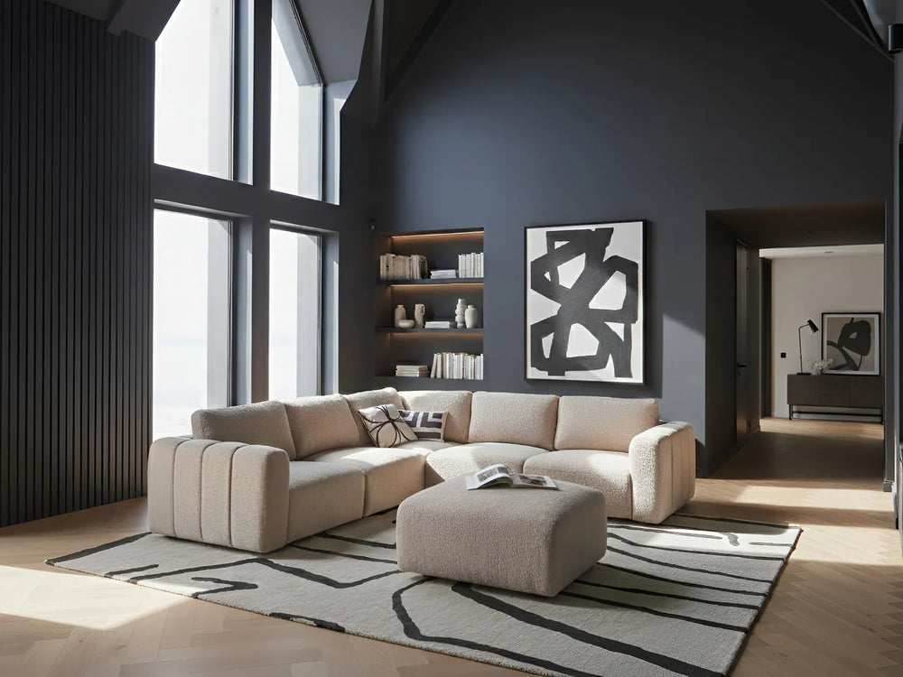 Modern living room with a beige sectional sofa, abstract art on the wall, and a rug.