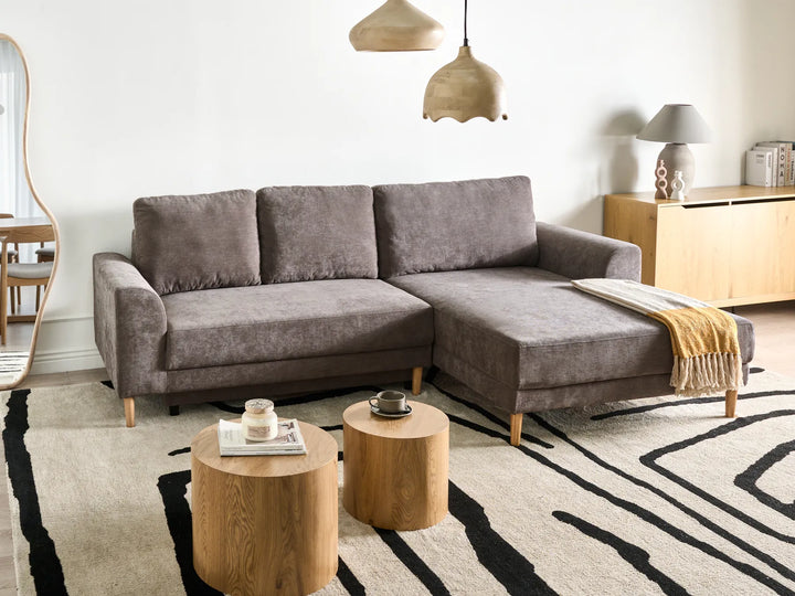 Gray sectional sofa in a living room with wooden side tables and a patterned rug.