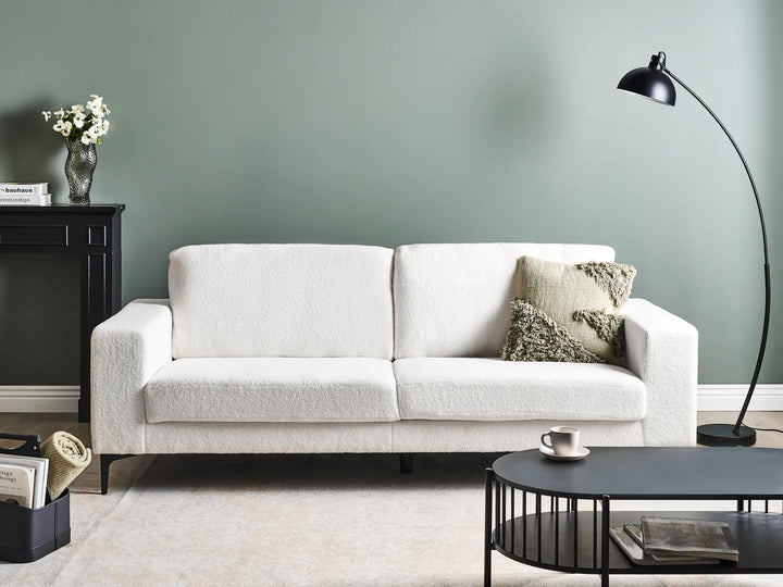 White sofa in a living room with a green wall, black floor lamp, and coffee table.