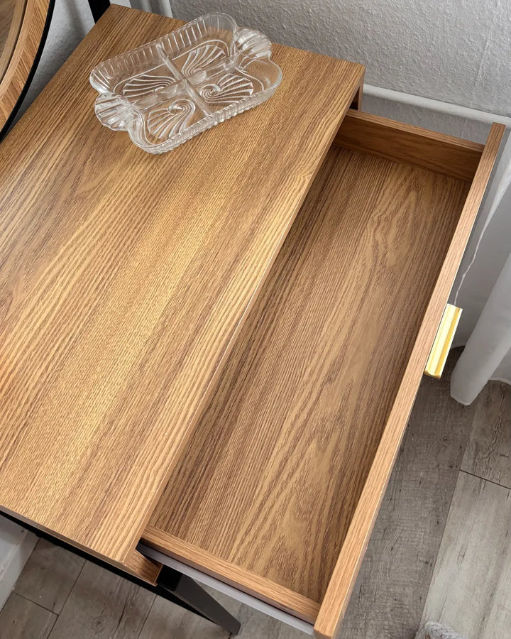 A light oak wood desk or dresser with an open drawer, showing a clear glass decorative tray resting on the desktop surface.