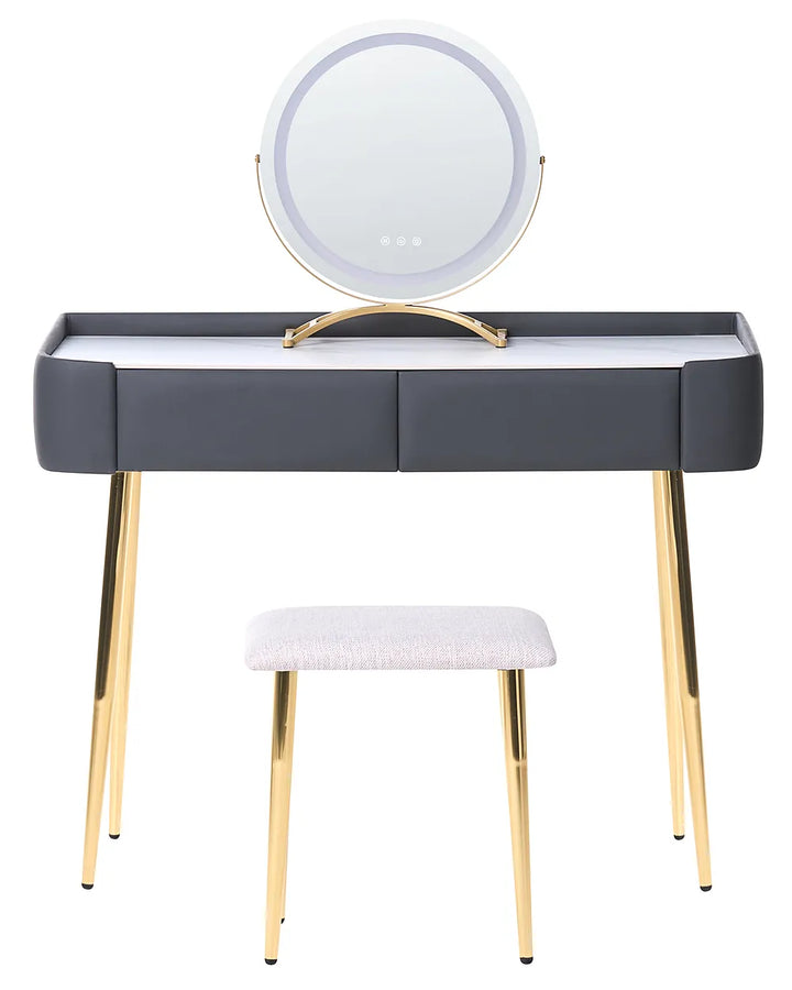 A modern vanity table set with a dark gray faux-leather desk, gold metal legs, a matching stool, and an illuminated round mirror on a white background.