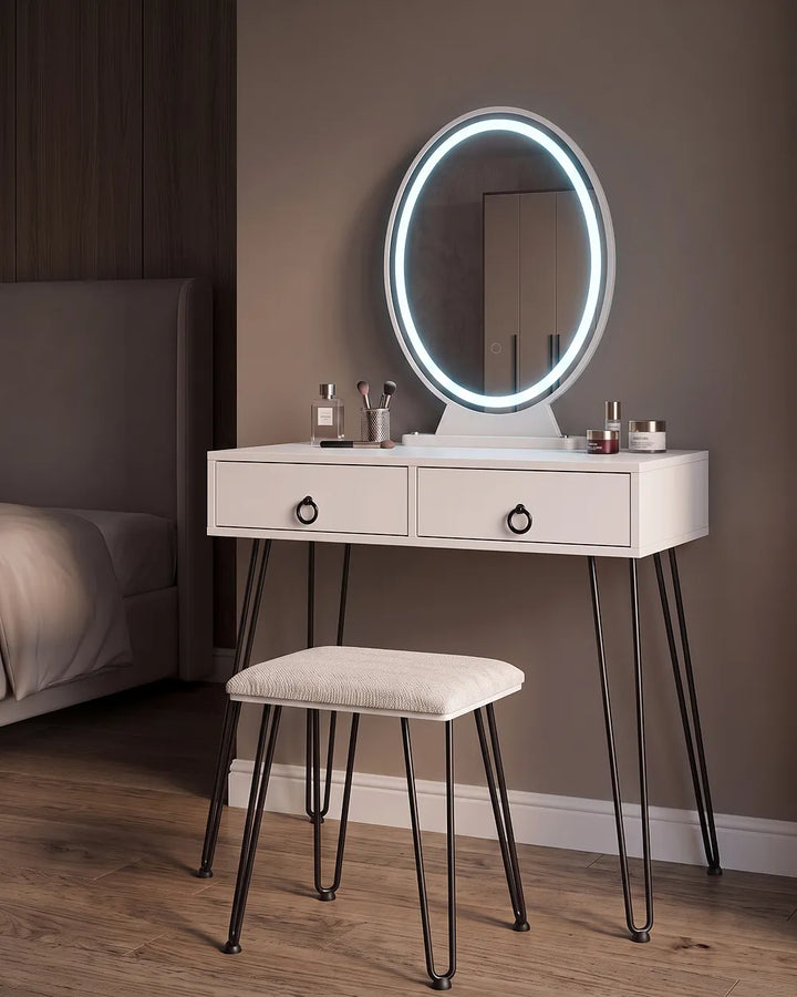 White vanity table with two drawers, black hairpin legs, and an oval LED-backlit mirror, shown with a matching stool in a bedroom setting.