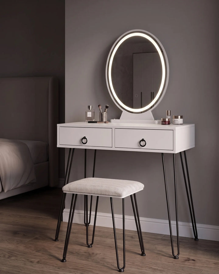 White vanity table with two drawers, black hairpin legs, and an oval LED-backlit mirror, shown in a bedroom setting with a matching stool.