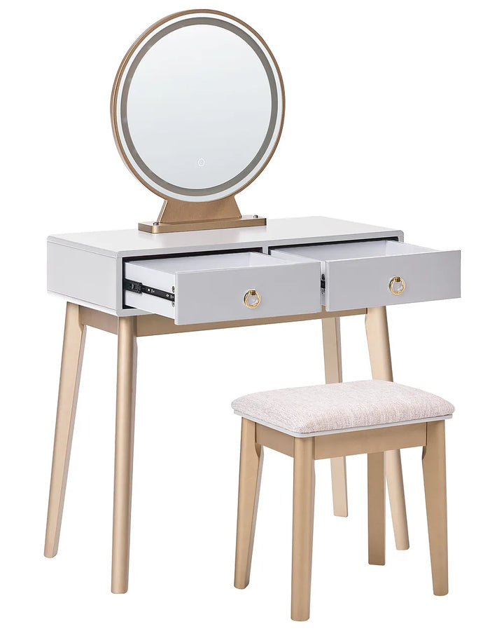 A modern vanity table set with a white top, light wood legs and frame, a round backlit mirror, two open drawers with gold ring pulls, and a matching upholstered stool on a white background.