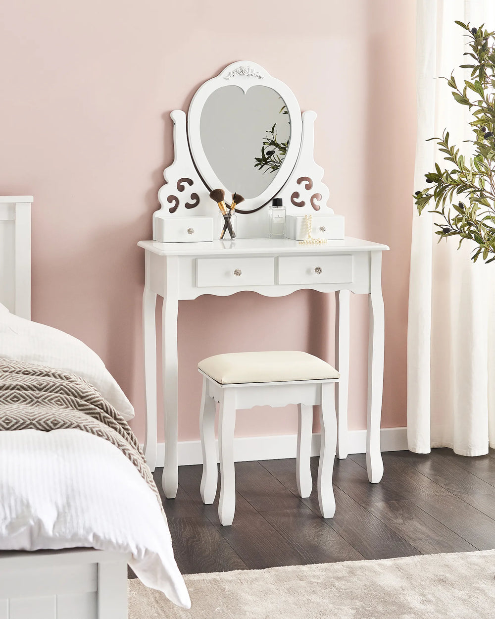 White vanity table with mirror and stool against a pink wall in a bedroom setting.