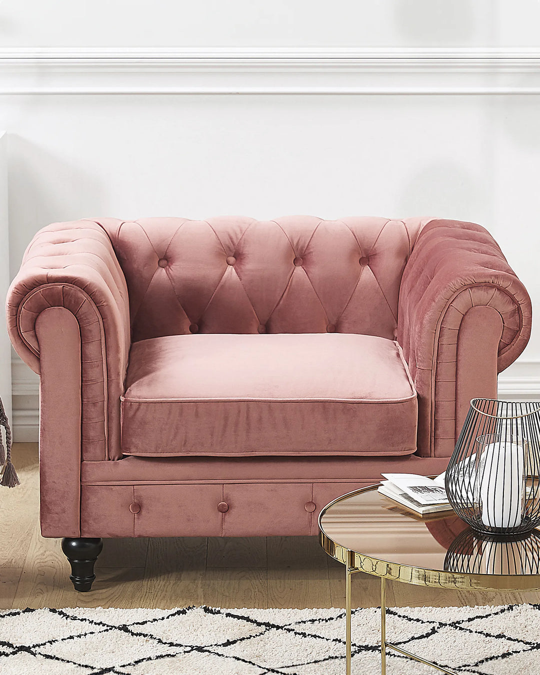 Pink velvet armchair in a stylish room with a round table and decorative items.