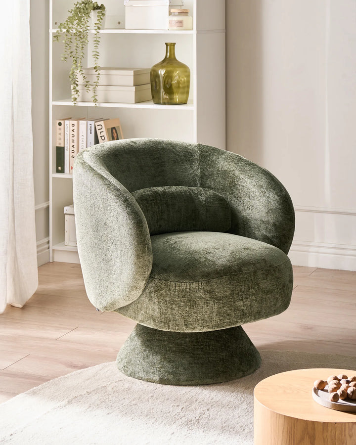 Green velvet chair in a living room setting with a bookshelf and small table.