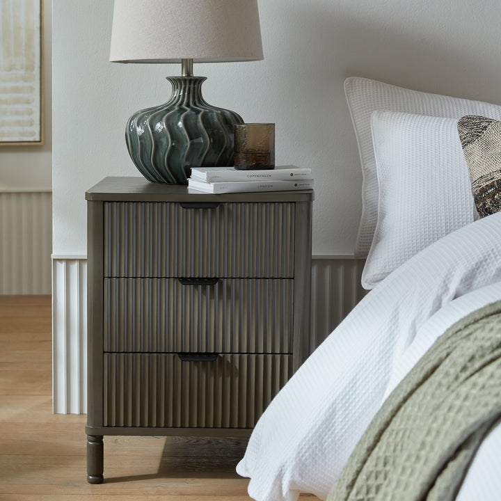 Gray nightstand with lamp and books next to a bed in a bedroom setting