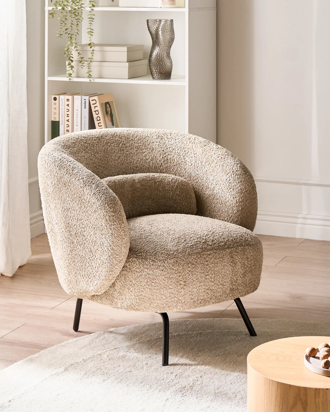 Beige textured armchair in a living room setting with a bookshelf and coffee table.