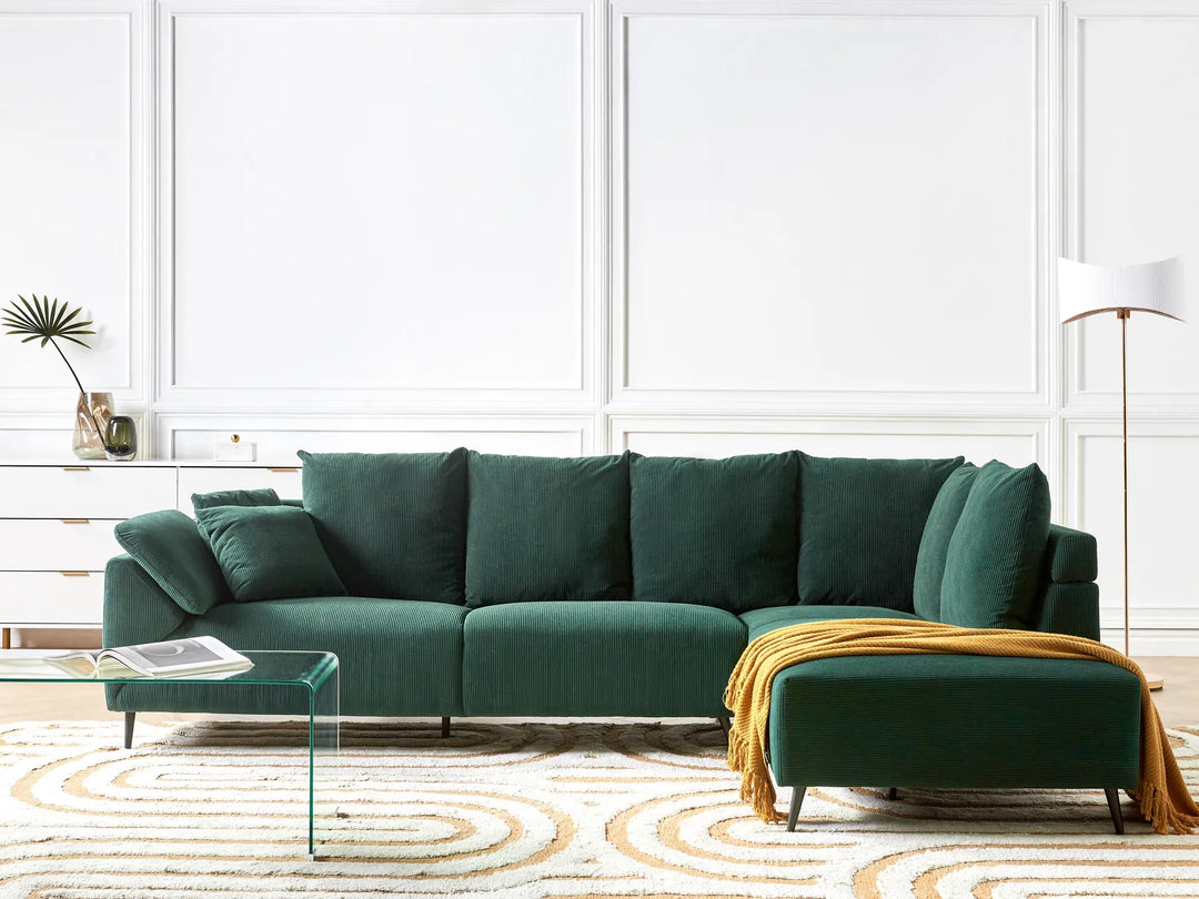 Green sectional sofa in a living room with a white wall and decorative elements.
