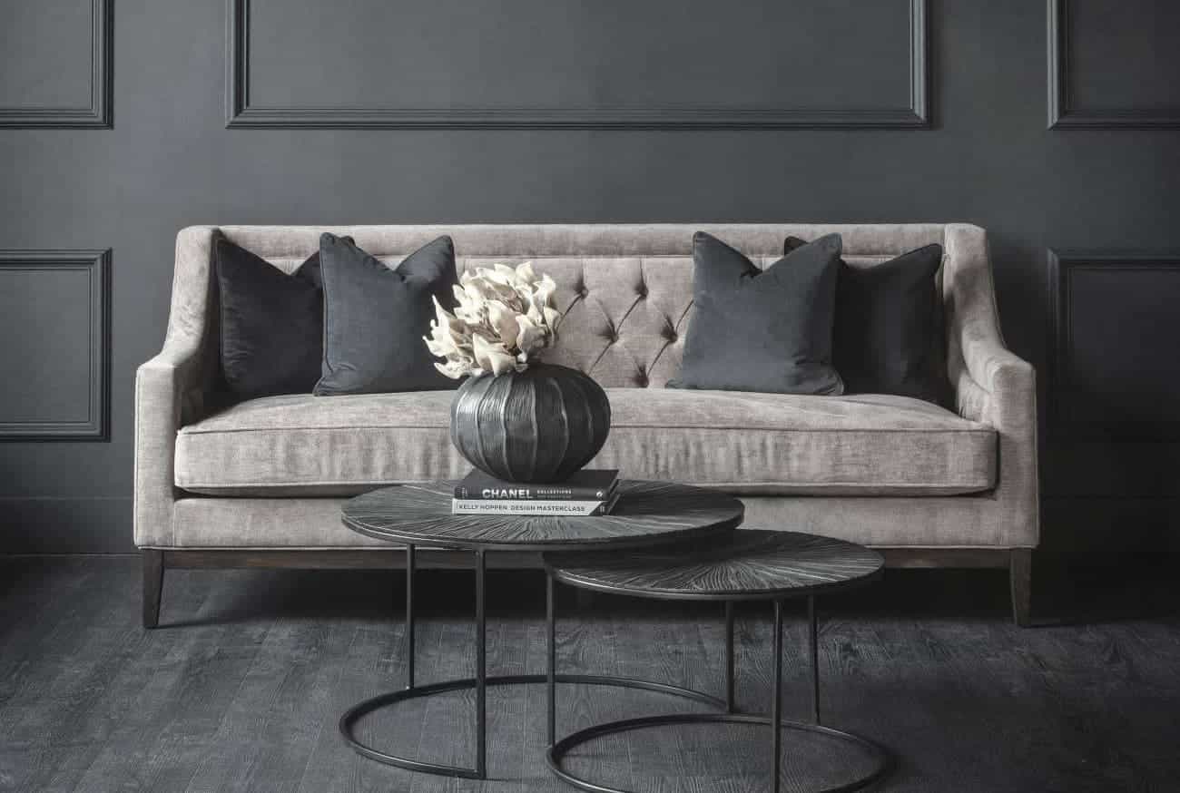 Gray tufted sofa with dark cushions in a room with dark gray walls and flooring.