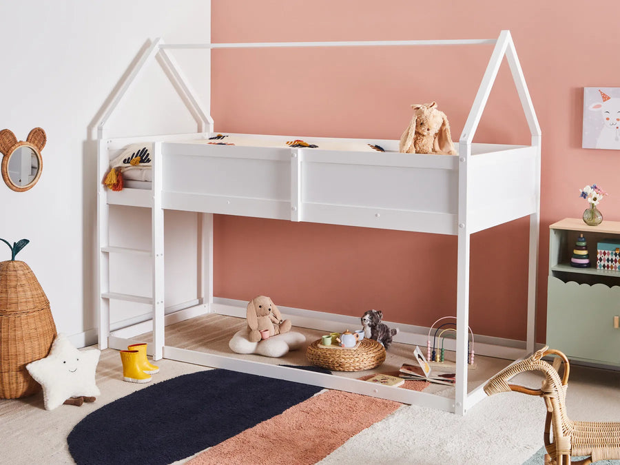 Children's room with a white house-shaped bed, toys, and a pink wall.