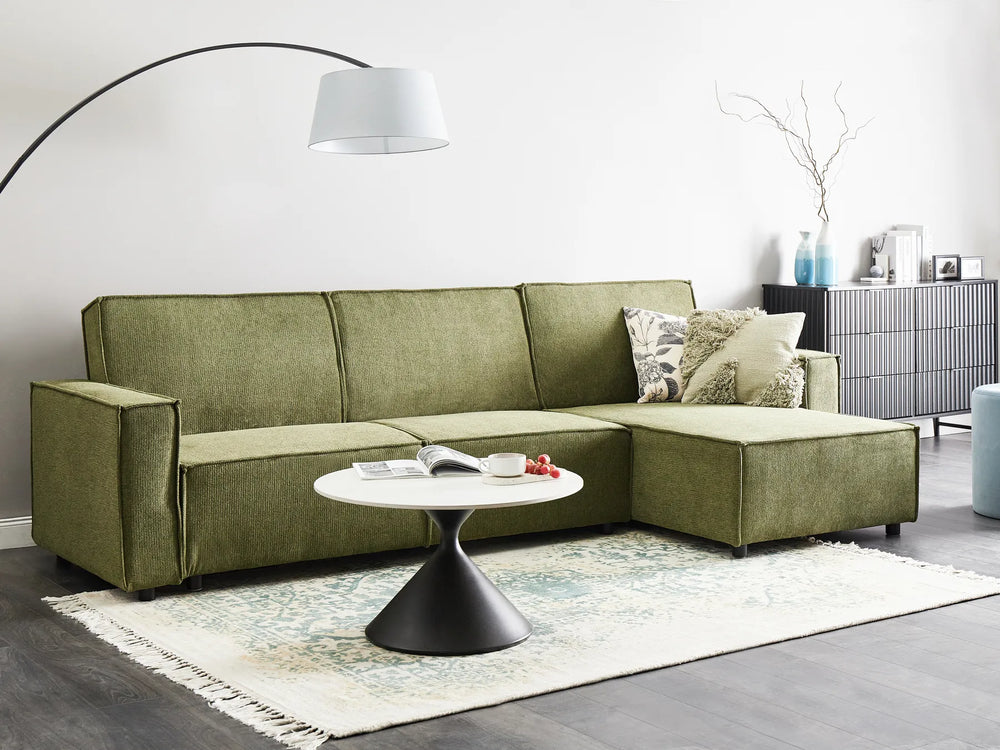 Green sectional sofa in a living room with a white coffee table and decorative items.