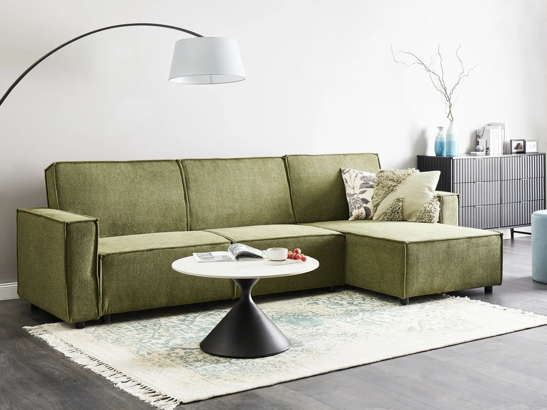 Green sectional sofa in a living room with a white coffee table and decorative items.