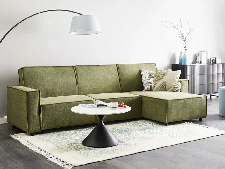 Green sectional sofa in a living room with a white coffee table and decorative items.