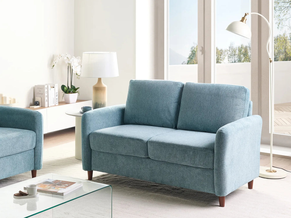 Blue sofa in a modern living room with a glass coffee table and decor items.