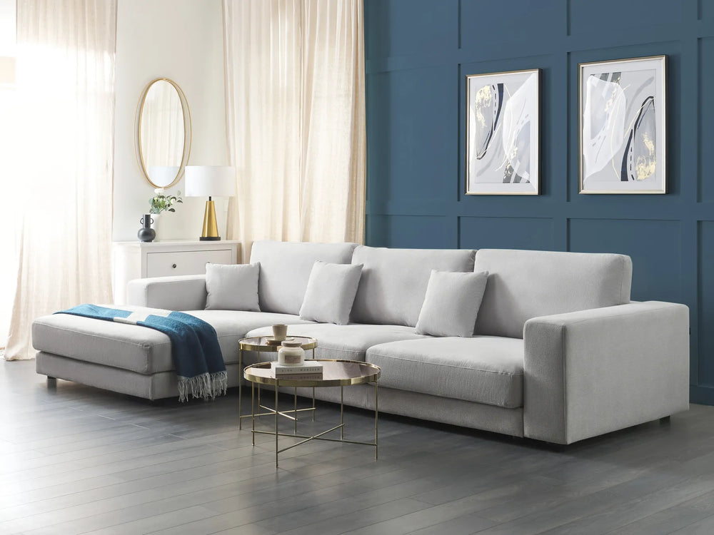 Gray sectional sofa in a living room with blue walls, white curtains, and decorative items.