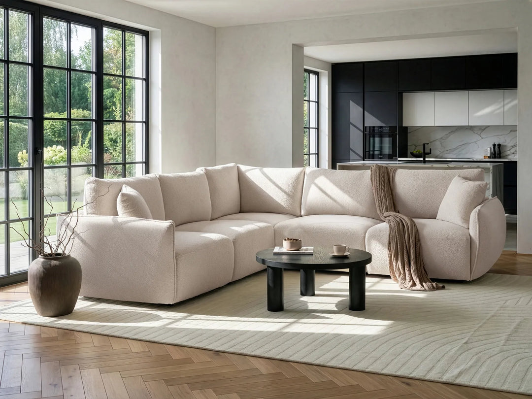 Modern living room with a beige sectional sofa, coffee table, and kitchen in the background.