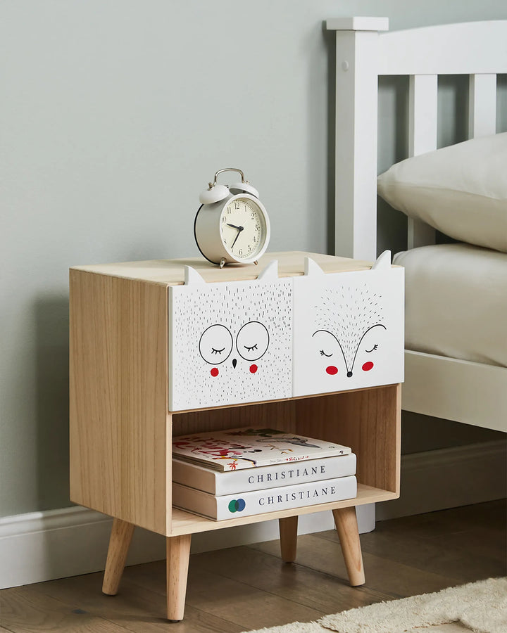 Wooden nightstand with white drawers, books, and an alarm clock in a bedroom setting.