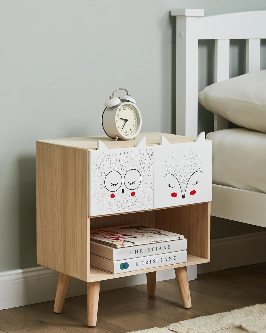 Wooden nightstand with white drawers, books, and an alarm clock in a bedroom setting.
